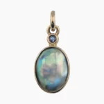 Pendant with a natural oval abalone pearl measuring 15 x 17mm from Mendocino, California set in solid 14-karat yellow gold with a 3mm round 0.11-carat accent sapphire at the top.