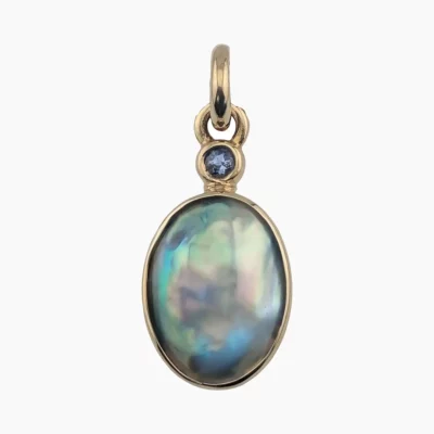 Pendant with a natural oval abalone pearl measuring 15 x 17mm from Mendocino, California set in solid 14-karat yellow gold with a 3mm round 0.11-carat accent sapphire at the top.