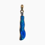 Pendant featuring a 2.5-carat freeform opal measuring 24 x 5mm from Coober Pedy, Australia. Set in 14-karat yellow gold with a round 2.4mm 0.05-carat VS1G diamond accent at the top.
