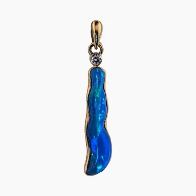 Pendant featuring a 2.5-carat freeform opal measuring 24 x 5mm from Coober Pedy, Australia. Set in 14-karat yellow gold with a round 2.4mm 0.05-carat VS1G diamond accent at the top.