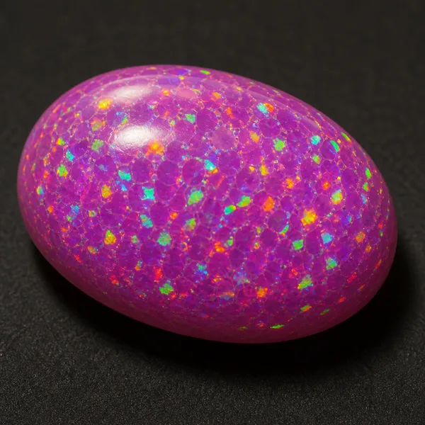 Lab-created synthetic opal cabochon in vivid uniform pink-purple with a regular columnar mosaic pattern under magnification